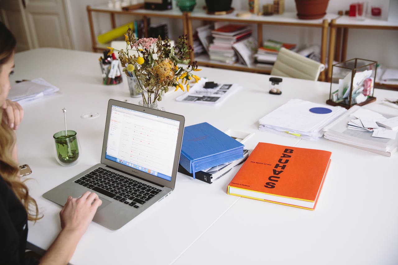 About Woman works on a laptop in a stylish office, surrounded by books and documents.