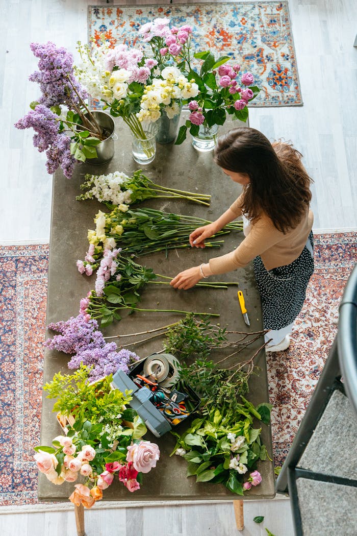 About Woman arranging a vibrant flower bouquet on a wooden table in a studio setting.
