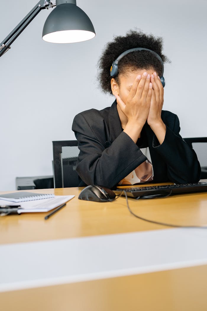 Services A tired call center employee covering her face with hands in frustration, wearing a headset in an office.